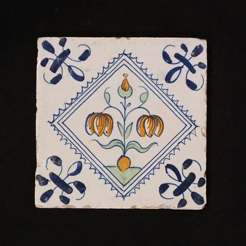 Polykromdekoreret hollandsk flise med 
blomstermotiv. Cirka 1620-40. Mål: 13x13cm