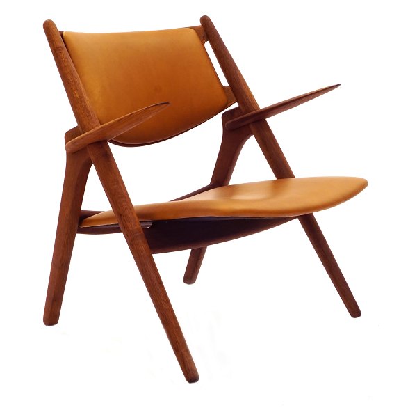 Hans Wegner Savbukkestol CH28. Hans J. Wegner, 1914-2007, Savbukkestol med 
armlæn i patineret eg med cognac farvet læder. Fremstår i flot stand, 
nypolstret, med anilinlæder.